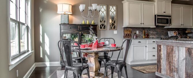 Modern kitchen-dining area with rustic accents by Pratt Home Builders in Chattanooga TN, featuring a wooden table, red dishware, and metal chairs.
