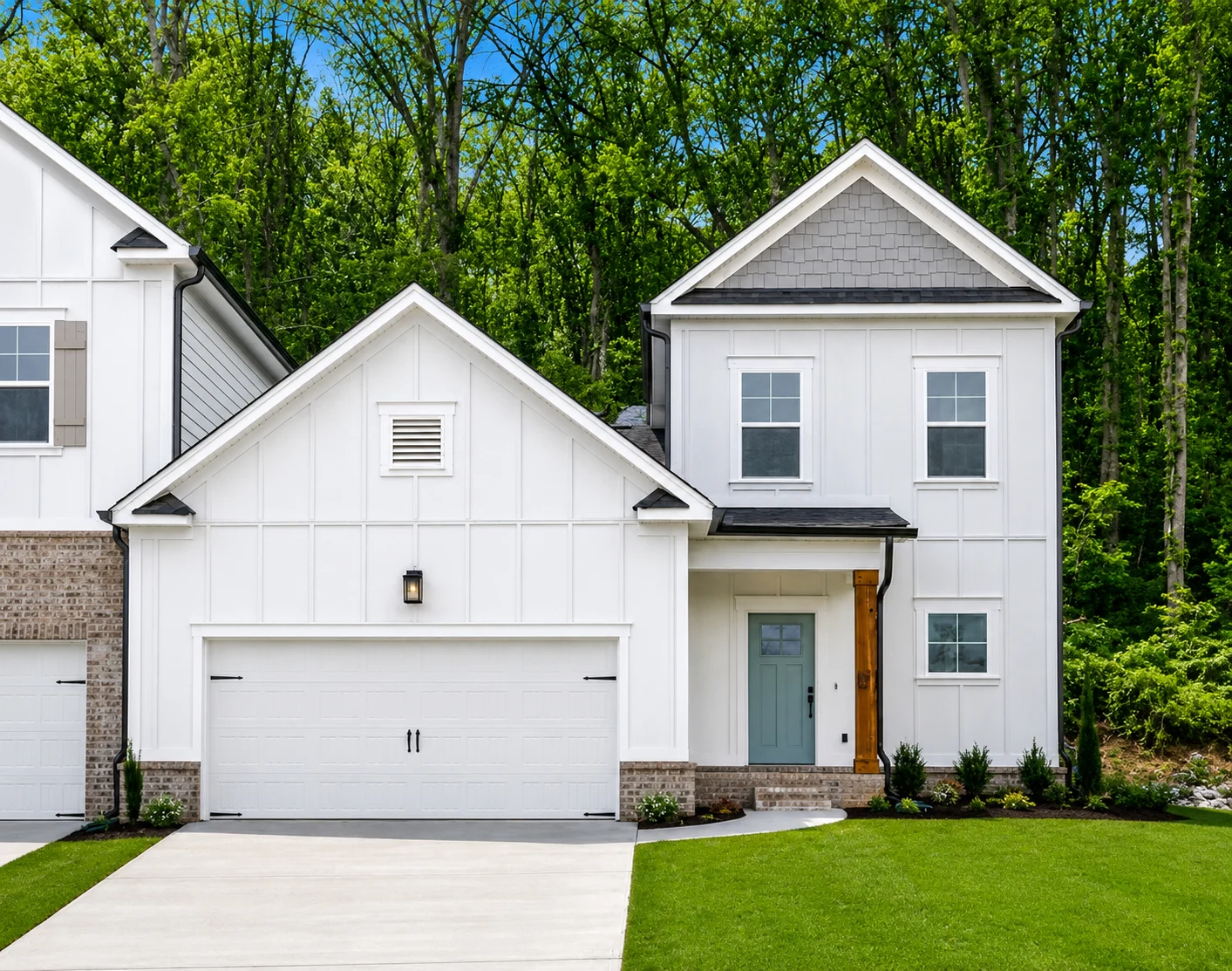 Altamont-floor-plan-front-exterior-hixson-townhome Modern two-story home with white siding, brick accents, and a garage, built by Pratt Home Builders in Chattanooga, TN, set against lush greenery.