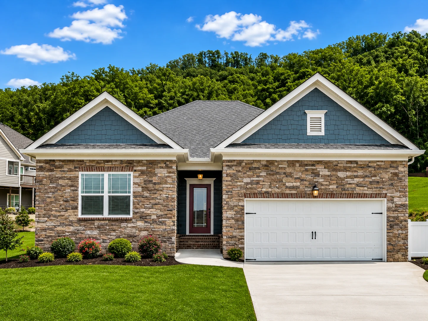 Primrose-floor-plan-front-exterior-home-for-sale Suburban house with stone facade, blue siding, and two-car garage, built by Pratt Home Builders in Chattanooga TN, set against lush green trees.