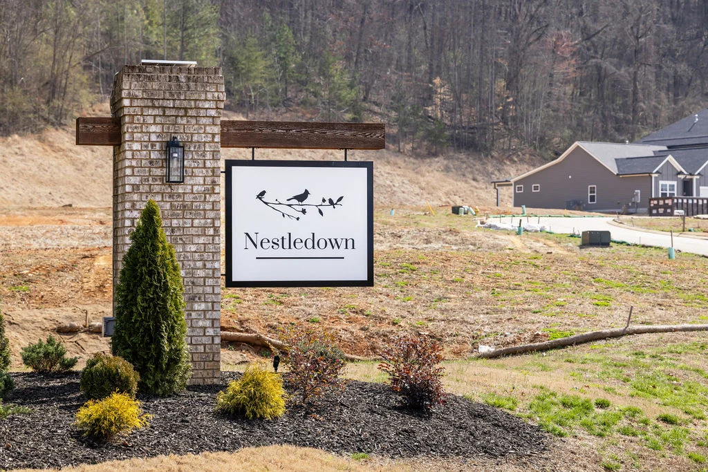 Sign for Nestledown community by Pratt Home Builders in Chattanooga TN, surrounded by shrubs and a developing residential area.