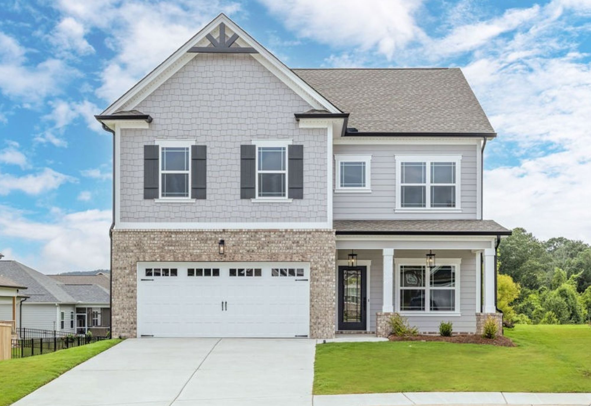 Two-story house with brick facade, white garage, and manicured lawn, by Pratt Home Builders in Chattanooga TN, under a blue sky.