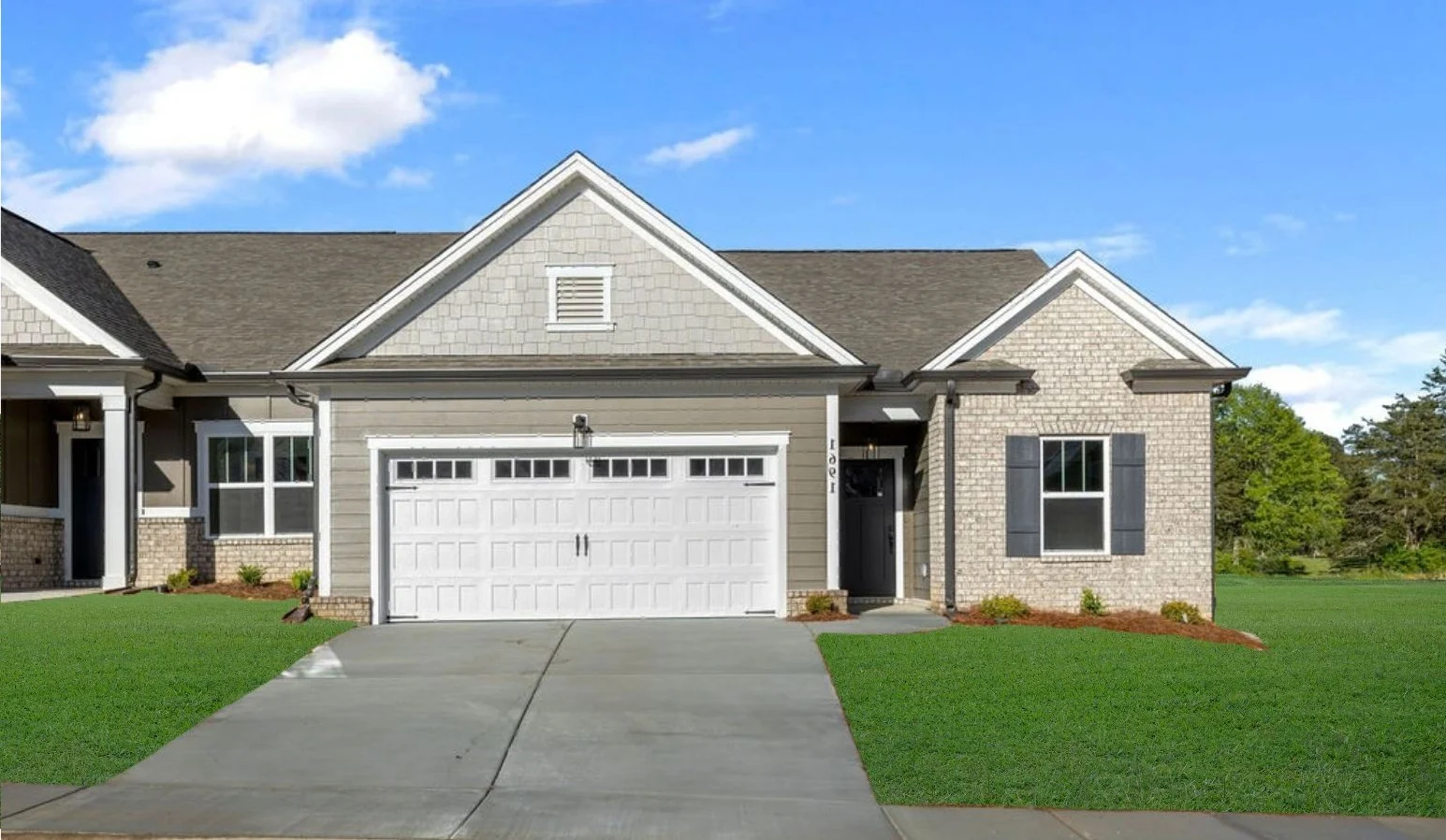 Single-story townhome with gable roof, brick facade, and white garage by Pratt Home Builders, surrounded by green lawn.