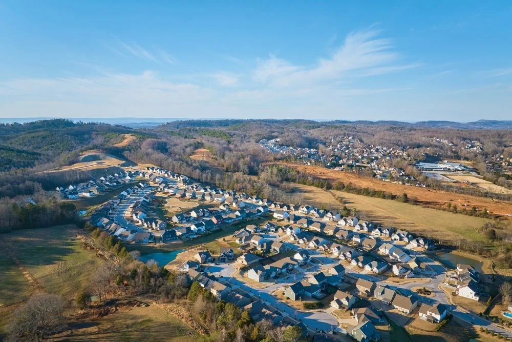 Aerial view of a suburban neighborhood by Pratt Home Builders in Chattanooga, TN, nestled among scenic hills and greenery under a clear sky.