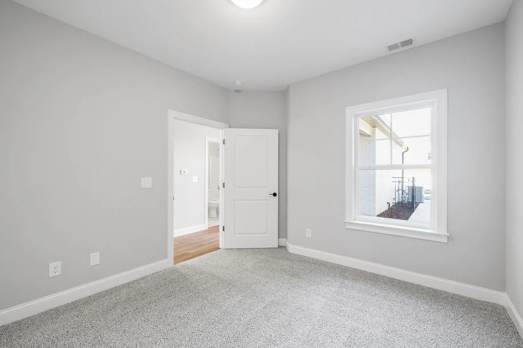 New Home Chattanooga TN. Bright, empty room with gray carpet, large window, and open door leading to hallway. Built by Pratt Home Builders.