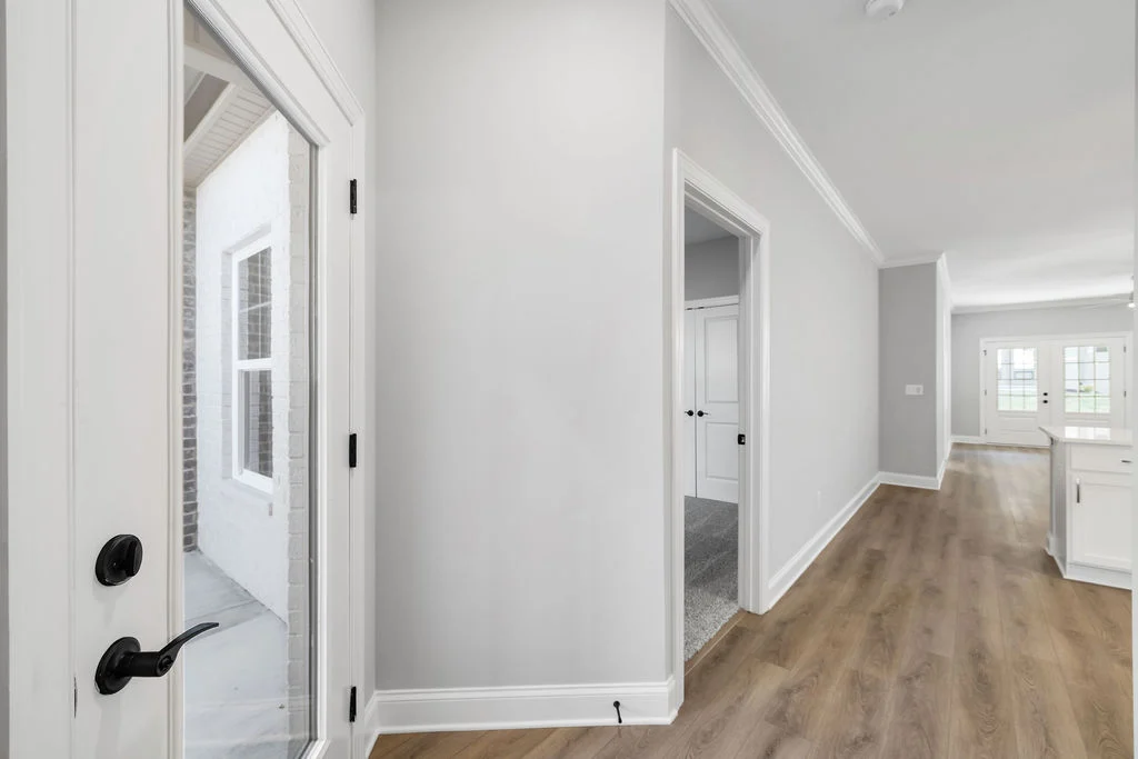 New Home Chattanooga TN. Bright hallway in a Pratt Home Builders house, featuring light wood floors, white walls, and a glass door.