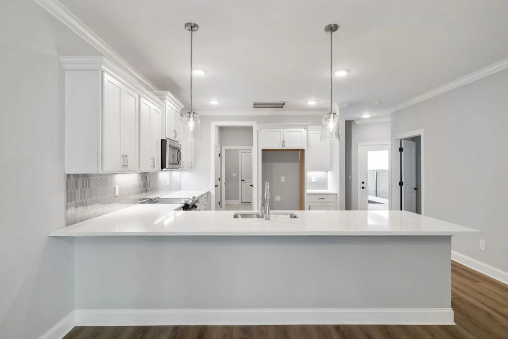 New Home Chattanooga TN. Modern kitchen by Pratt Home Builders, featuring white cabinets, a sleek island, and pendant lights over a hardwood floor.