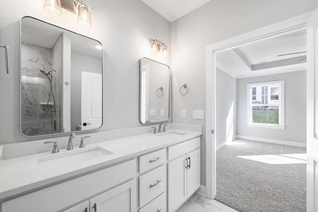 New Home Chattanooga TN. Modern bathroom with dual sinks, elegant mirrors, and a glimpse into a sunlit bedroom; designed by Pratt Home Builders.