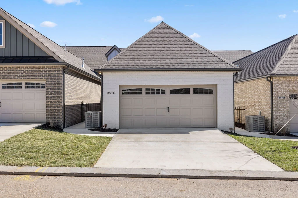 New Home Chattanooga TN. Garage with white brick exterior, gray door, by Pratt Home Builders, flanked by two homes, both with brick facades.
