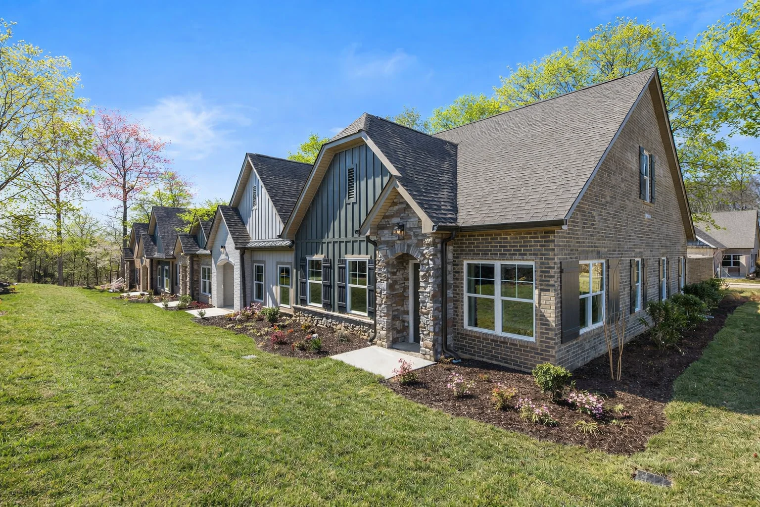 New Home Chattanooga TN. Row of charming brick townhomes with lush landscaping by Pratt Home Builders, under a clear blue sky.