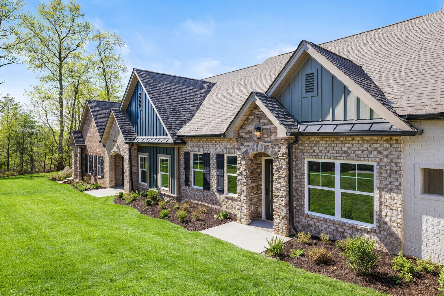 Modern home with stone and brick facade, lush lawn, and trees. Built by Pratt Home Builders in Chattanooga TN.