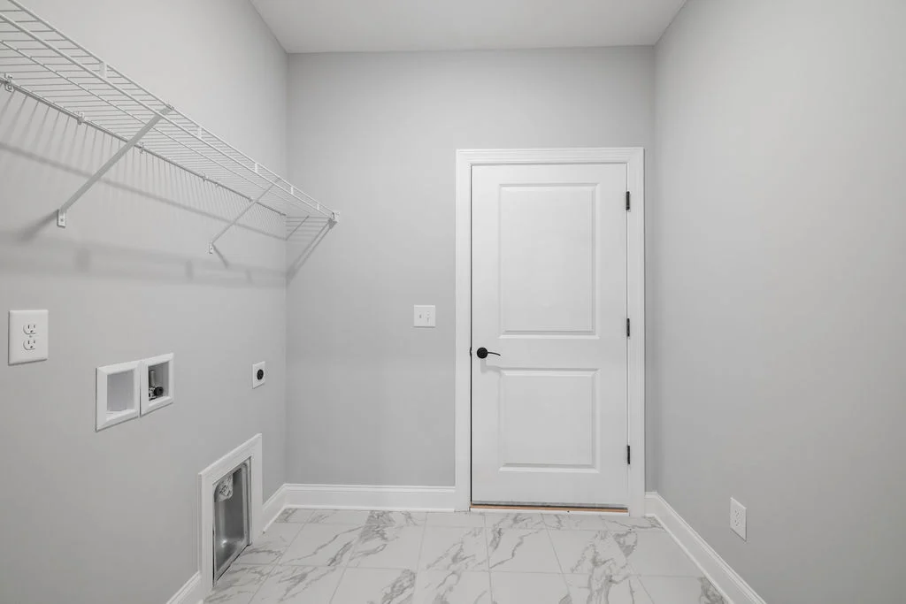 Laundry room with a white door, wire shelf, and utility hookups, featuring marble tile flooring by Pratt Home Builders in Chattanooga TN.
