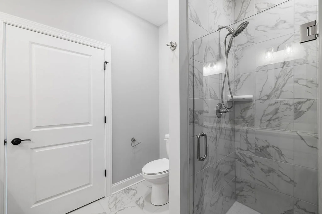 New Home Chattanooga TN. Modern bathroom with marble-tiled shower and glass door by Pratt Home Builders, featuring sleek fixtures and soft lighting.