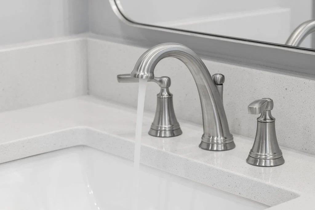 Modern faucet with water running over a white countertop; design by Pratt Home Builders in Chattanooga TN.