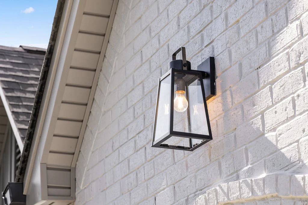 Modern black lantern-style outdoor light fixture on a white brick wall, showcasing Pratt Home Builders in Chattanooga TN craftsmanship.