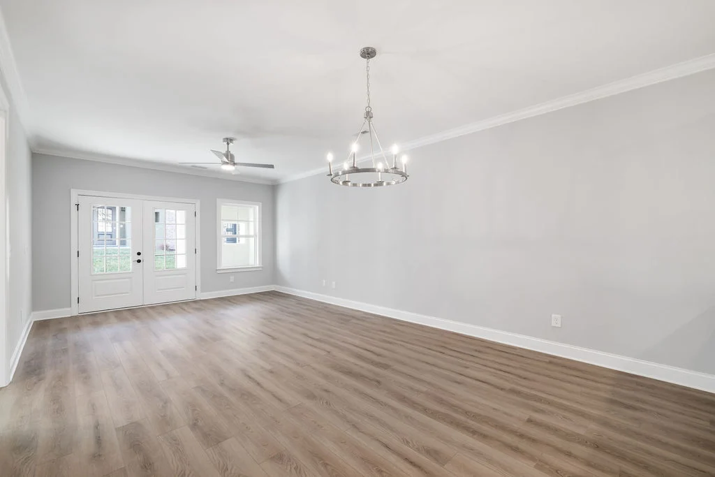 Spacious, empty living room with light wood floors, modern chandelier, white double doors, and ceiling fan. Built by Pratt Home Builders in Chattanoog