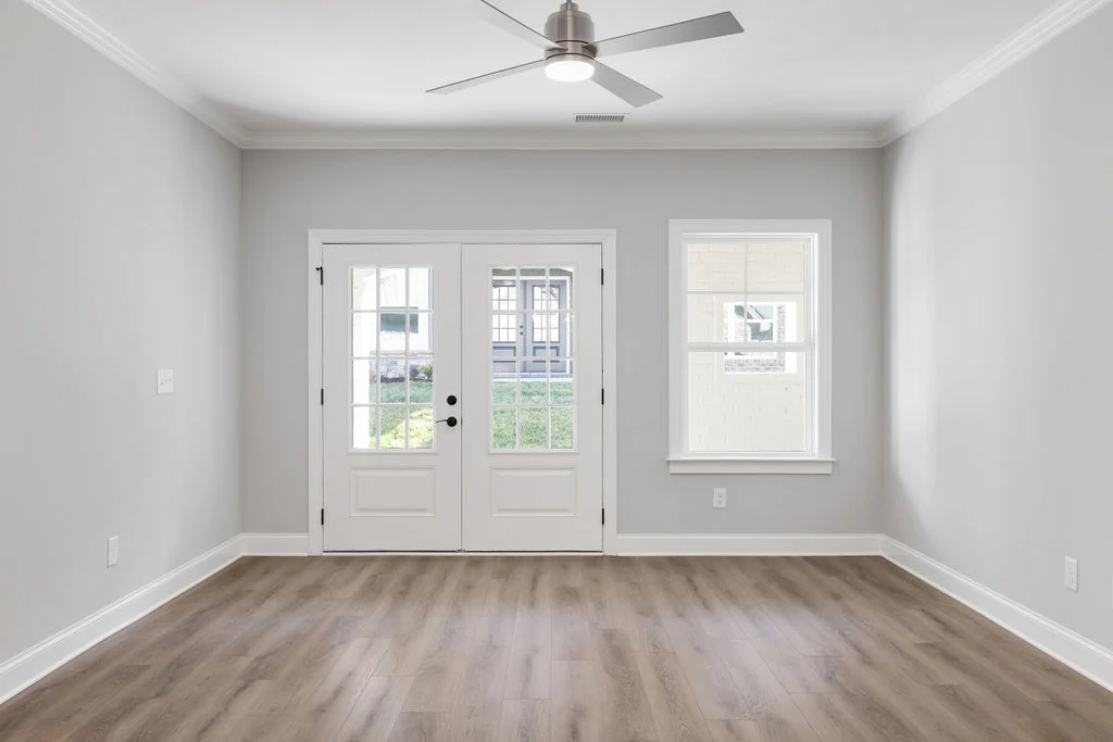Bright, empty room with light wood floor, ceiling fan, and glass double doors by Pratt Home Builders in Chattanooga TN, offering natural light.