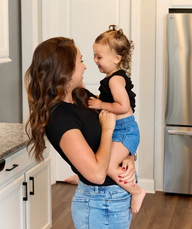 Designed for Real Life Woman holding a smiling toddler in a modern kitchen, showcasing Pratt Home Builders in Chattanooga TN.