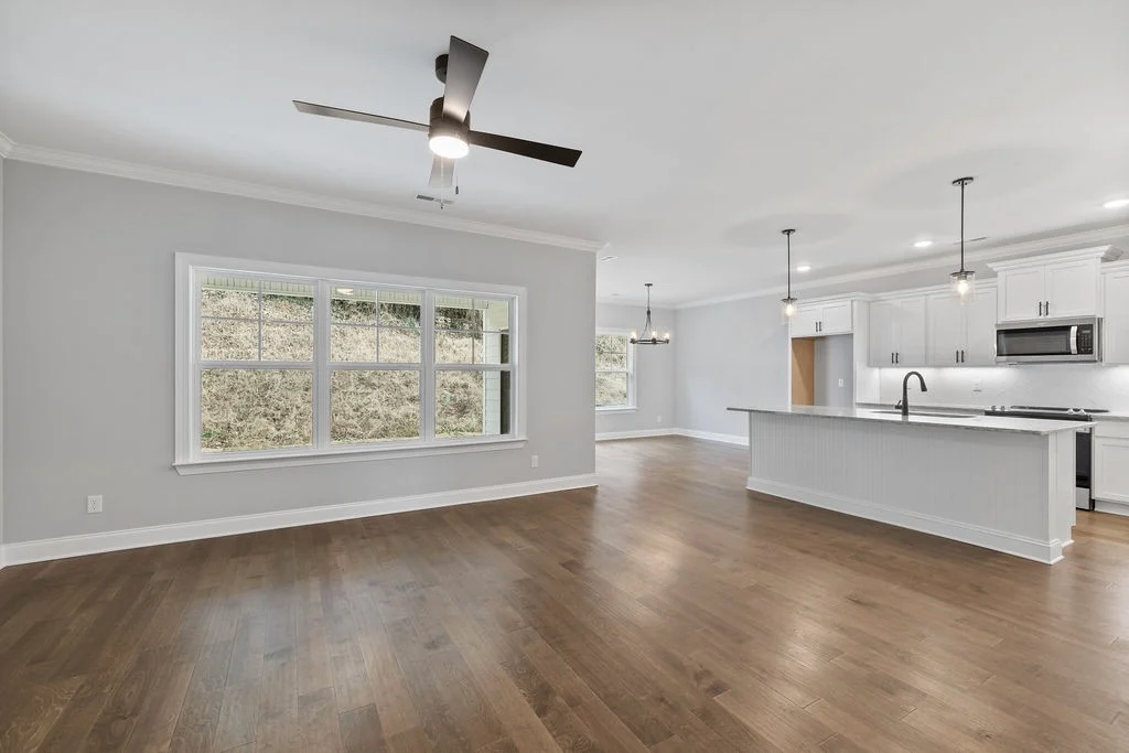 Spacious open-concept kitchen and living area with white cabinets, island, modern lighting, and hardwood floors by Pratt Home Builders in Chattanooga
