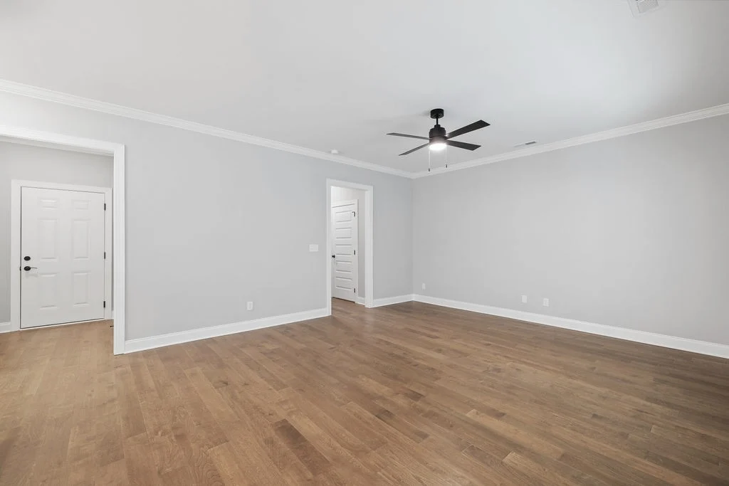 Spacious empty room with hardwood floors, gray walls, ceiling fan, and two white doors, showcasing Pratt Home Builders in Chattanooga TN.