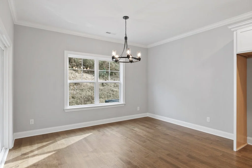 Bright, empty dining room with hardwood floors, gray walls, large window, and elegant chandelier. Built by Pratt Home Builders in Chattanooga TN.