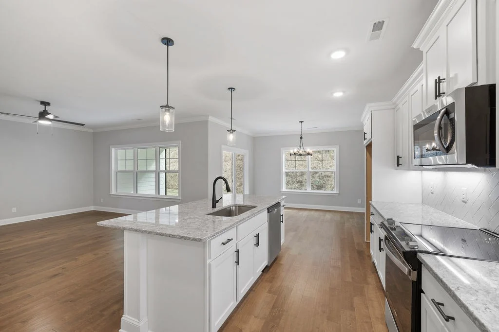 Modern kitchen and living area with hardwood floors, elegant lighting, and white cabinetry by Pratt Home Builders in Chattanooga TN.
