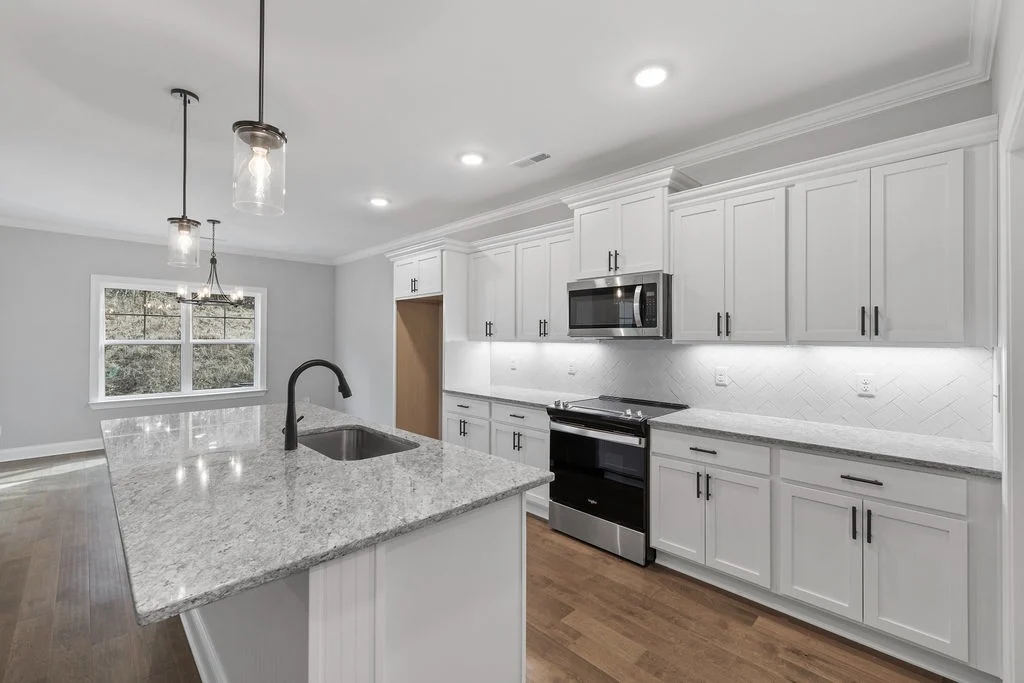 Modern kitchen by Pratt Home Builders in Chattanooga TN features white cabinetry, granite countertops, and pendant lighting over an island sink.