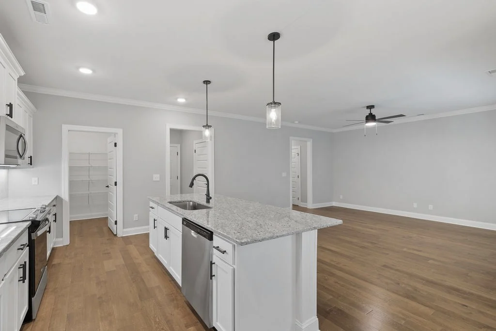 Modern kitchen and living area with hardwood floors, granite countertops, stainless appliances, and pendant lighting by Pratt Home Builders in Chattan