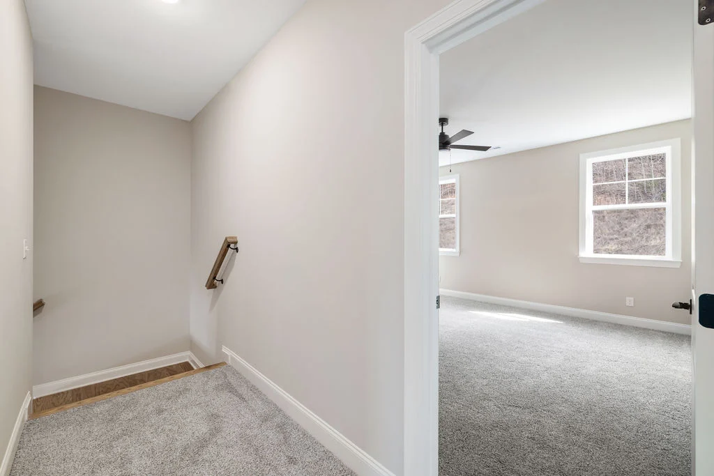 View of a stairway landing and a bright room with carpet, ceiling fan, and two windows. Pratt Home Builders in Chattanooga TN.