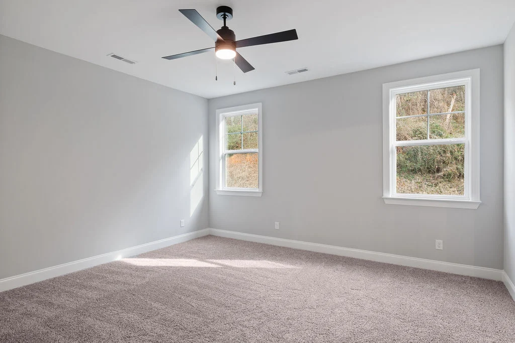 Bright, neutral room with light gray walls, plush carpet, ceiling fan, and two large windows by Pratt Home Builders in Chattanooga TN.