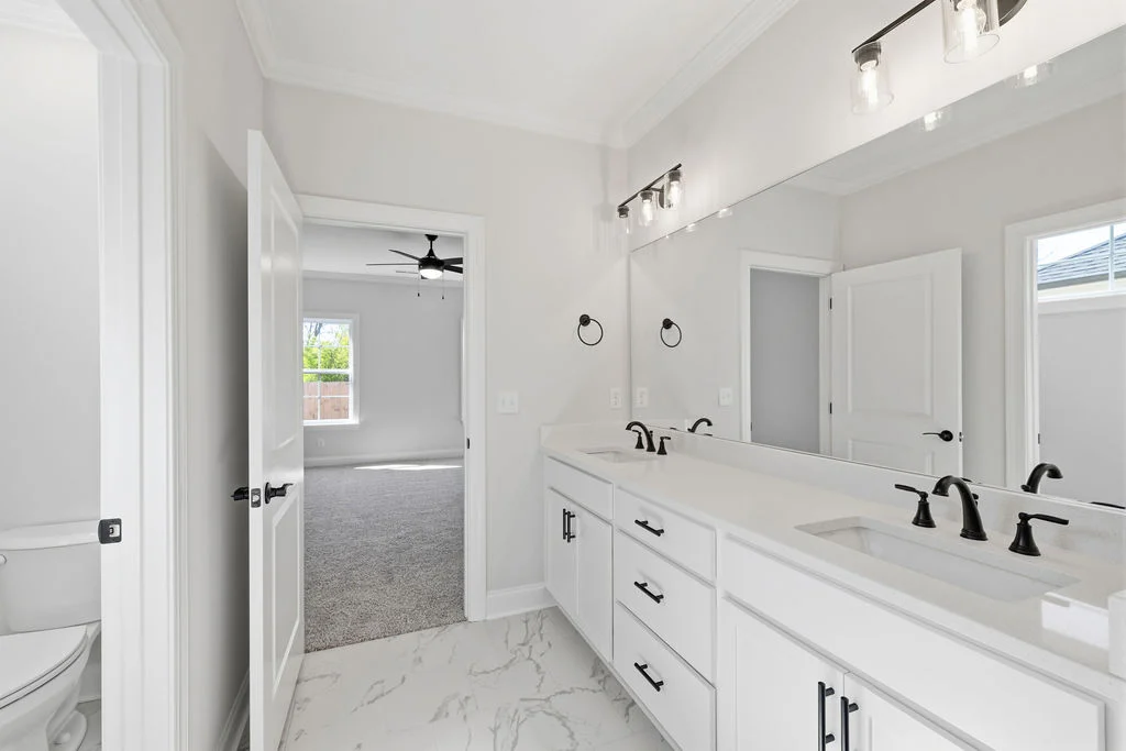 Bright bathroom featuring dual sinks, sleek black fixtures, marble floor, adjacent carpeted room. Pratt Home Builders in Chattanooga TN.
