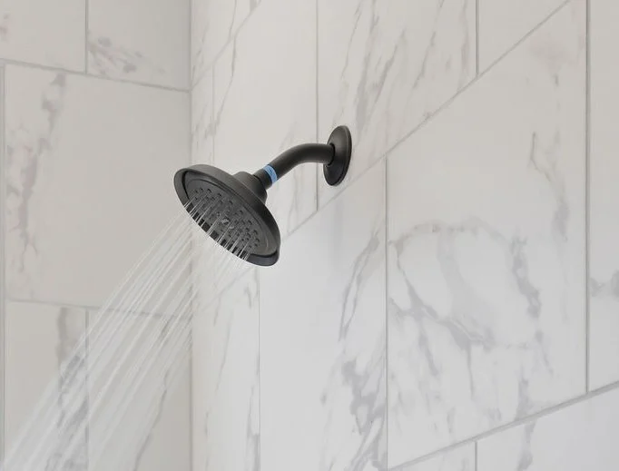 Black showerhead spraying water against marble-tiled wall, showcasing Pratt Home Builders in Chattanooga TN bathroom design.