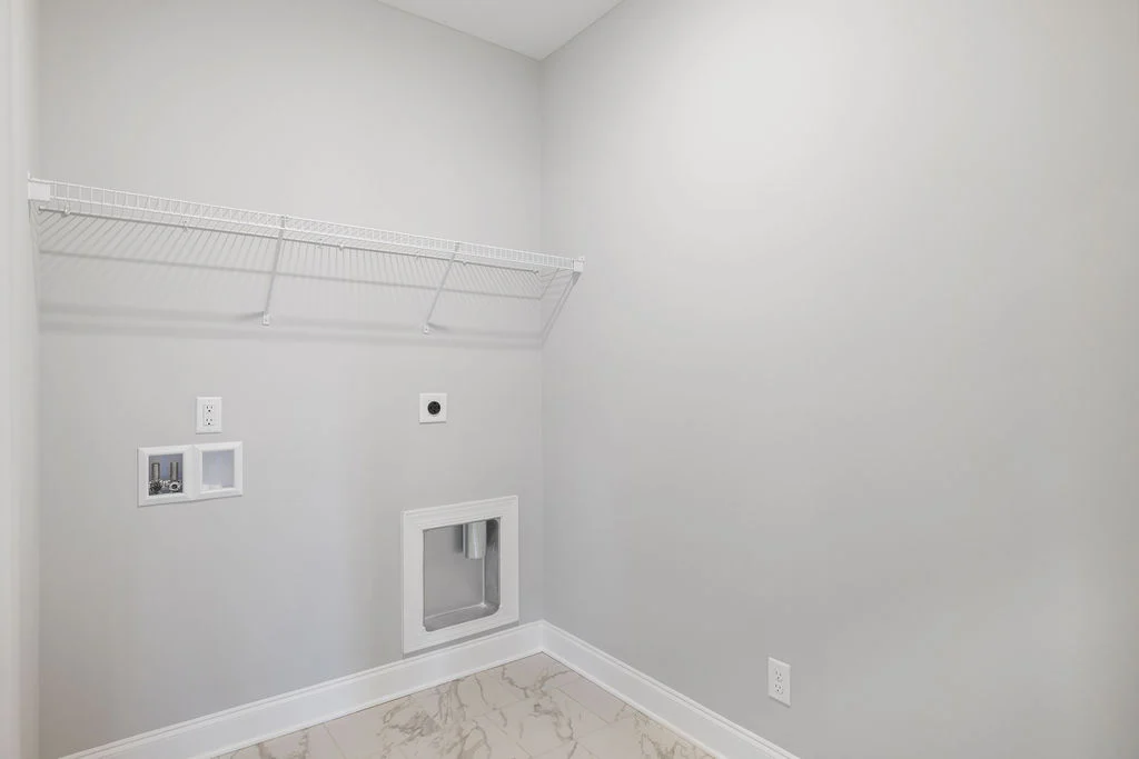 Bright, empty laundry room with white walls, marble floor, and wire shelf by Pratt Home Builders in Chattanooga TN.