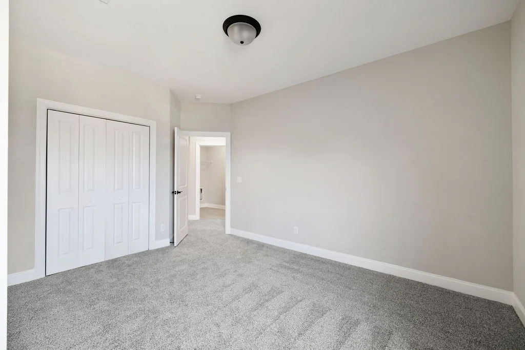 Empty beige-walled room with gray carpet, closet, and open door leading to hallway. Pratt Home Builders in Chattanooga TN craftsmanship.