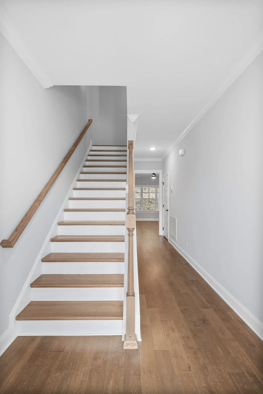 Entryway with wooden stairs and hallway leading to a well-lit room, designed by Pratt Home Builders in Chattanooga, TN.
