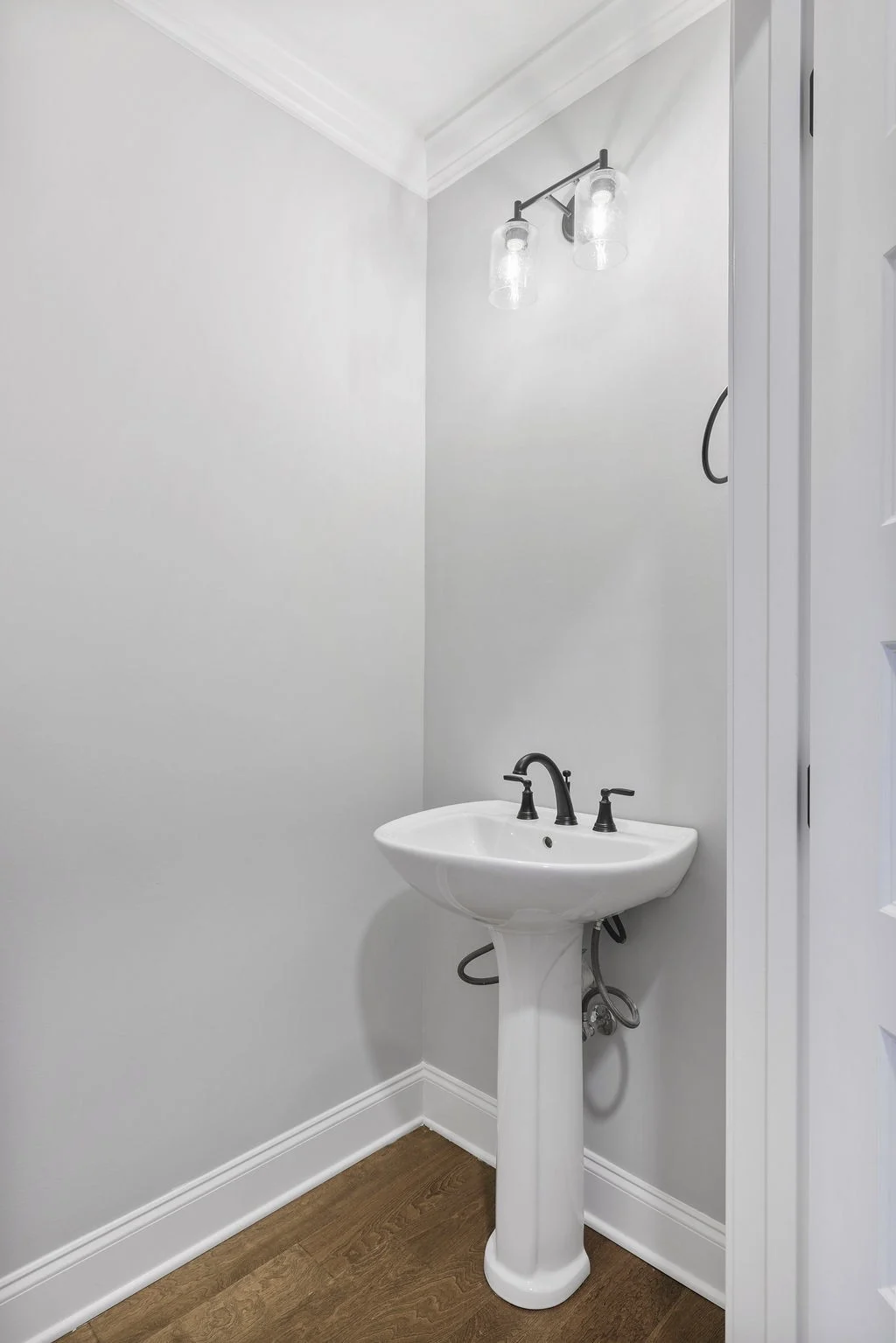 Small bathroom with a pedestal sink, dark faucets, and a double sconce light fixture by Pratt Home Builders in Chattanooga TN.
