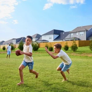 Boys Playing Football in Pratt yard Children playing football on lush green lawn with Pratt Home Builders houses in Chattanooga, TN visible in the background.