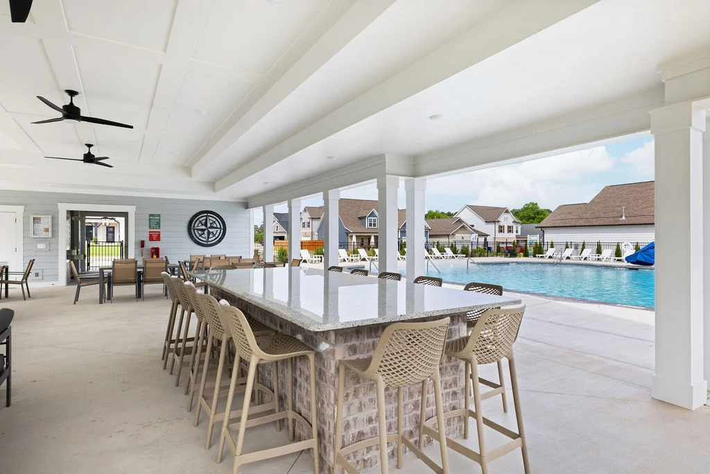 Covered patio with bar seating, ceiling fans, and a pool in the background, designed by Pratt Home Builders in Chattanooga TN.