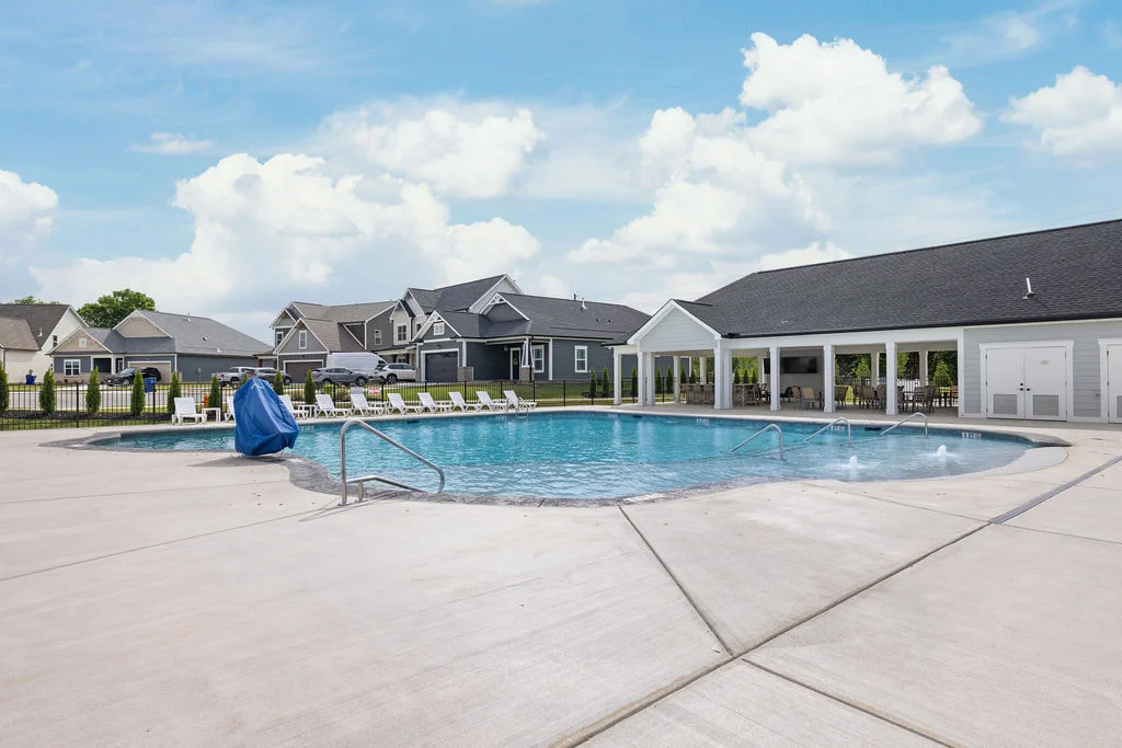 Community pool with surrounding lounge chairs and clubhouse, part of a neighborhood by Pratt Home Builders in Chattanooga, TN. Bright, sunny day.
