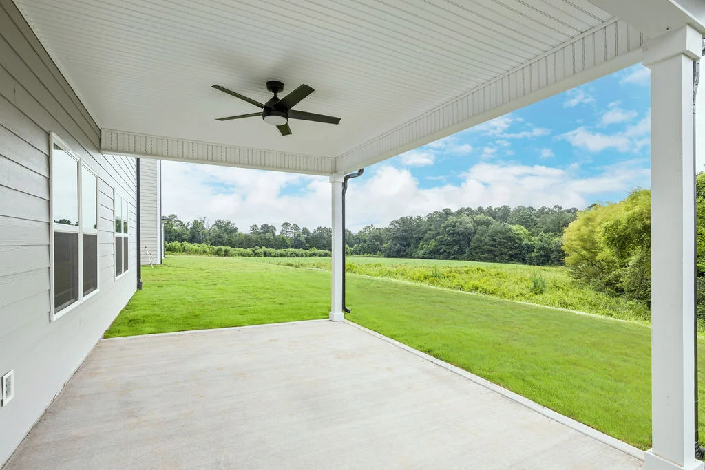 Covered patio with ceiling fan overlooking a lush green lawn and wooded area, designed by Pratt Home Builders in Chattanooga TN.