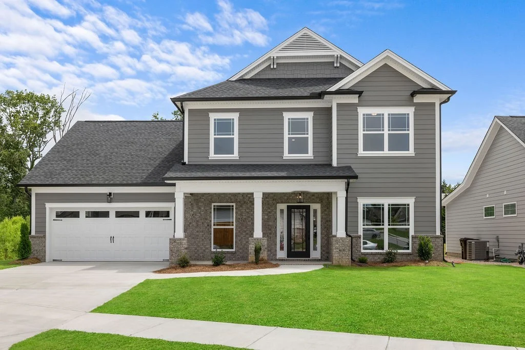 Two-story gray house with front porch and garage, built by Pratt Home Builders in Chattanooga, TN, surrounded by green lawn and blue sky.