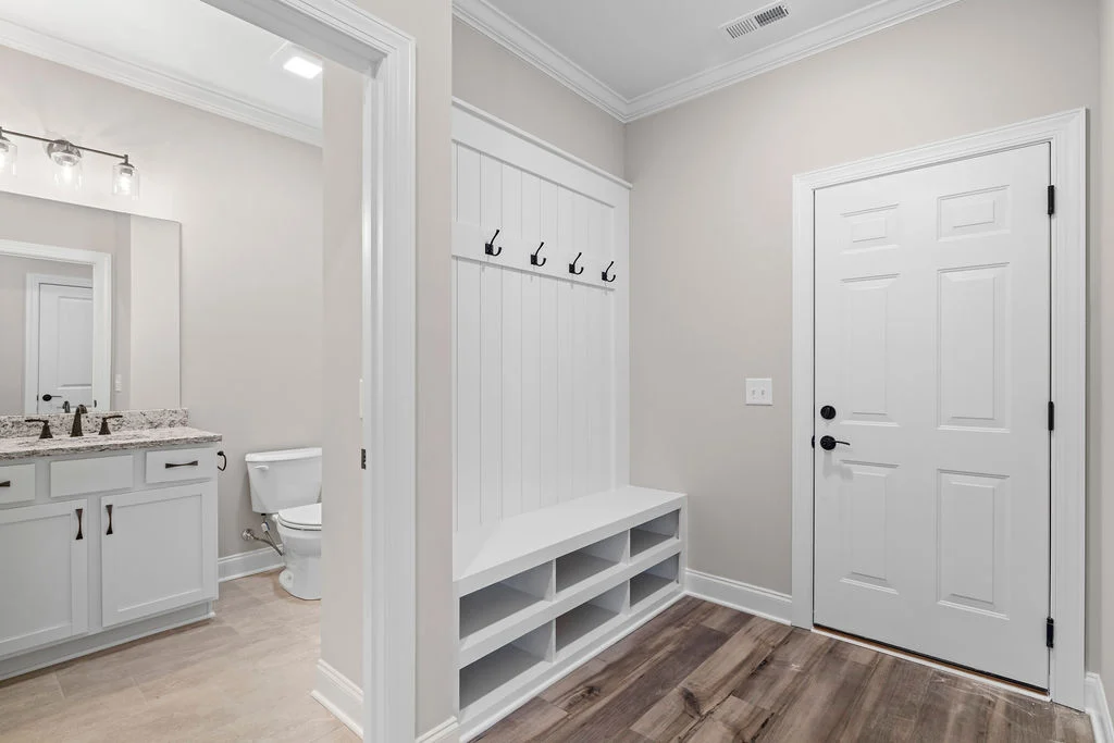 White hallway with bench, coat hooks, and wooden floor near bathroom featuring double vanity. Pratt Home Builders in Chattanooga TN.