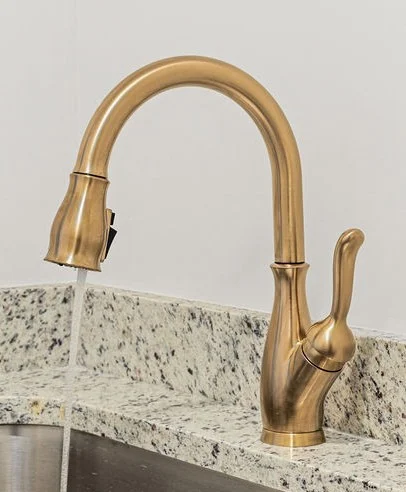 Elegant bronze kitchen faucet with running water, set against a speckled granite countertop, featured by Pratt Home Builders in Chattanooga TN.