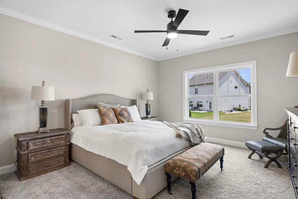 Elegant bedroom with neutral tones, cozy bed, wooden nightstand, large window view. Designed by Pratt Home Builders in Chattanooga TN.