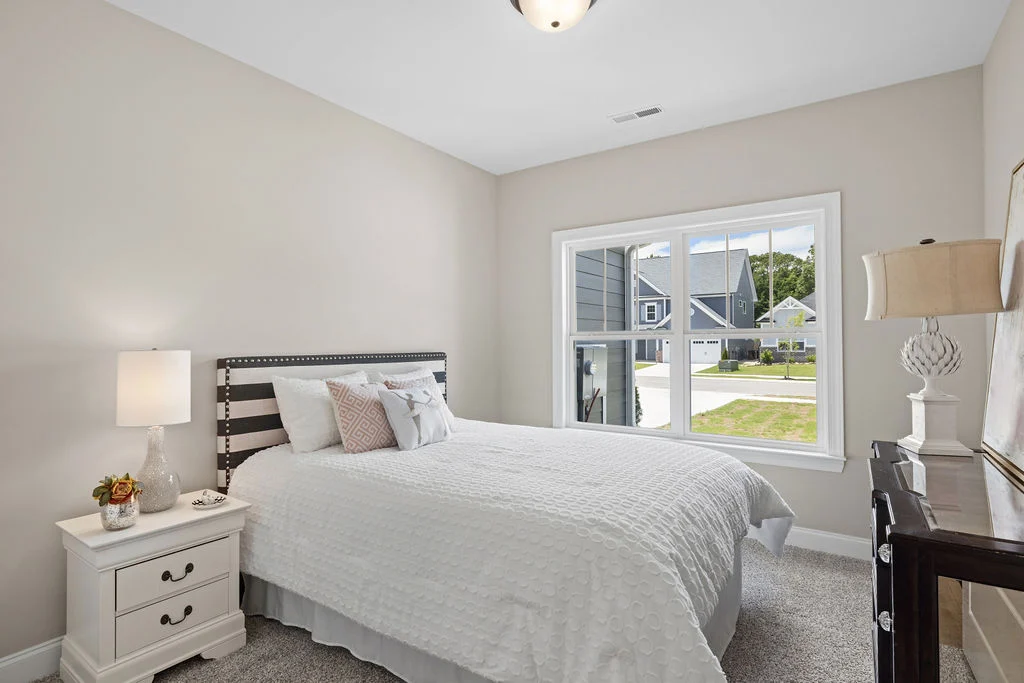 Cozy bedroom with striped headboard, white bedding, and lamps on nightstands. Sunny view through windows. Built by Pratt Home Builders in Chattanooga