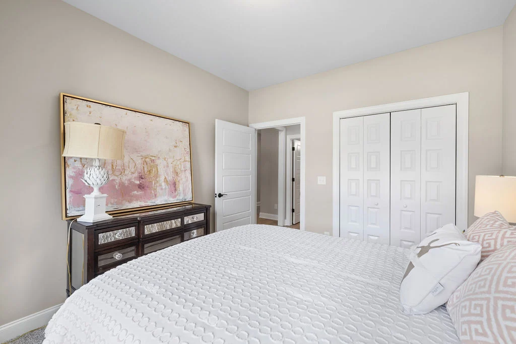 Cozy bedroom by Pratt Home Builders in Chattanooga TN, featuring a textured bedspread, patterned pillows, a dresser, and abstract wall art.