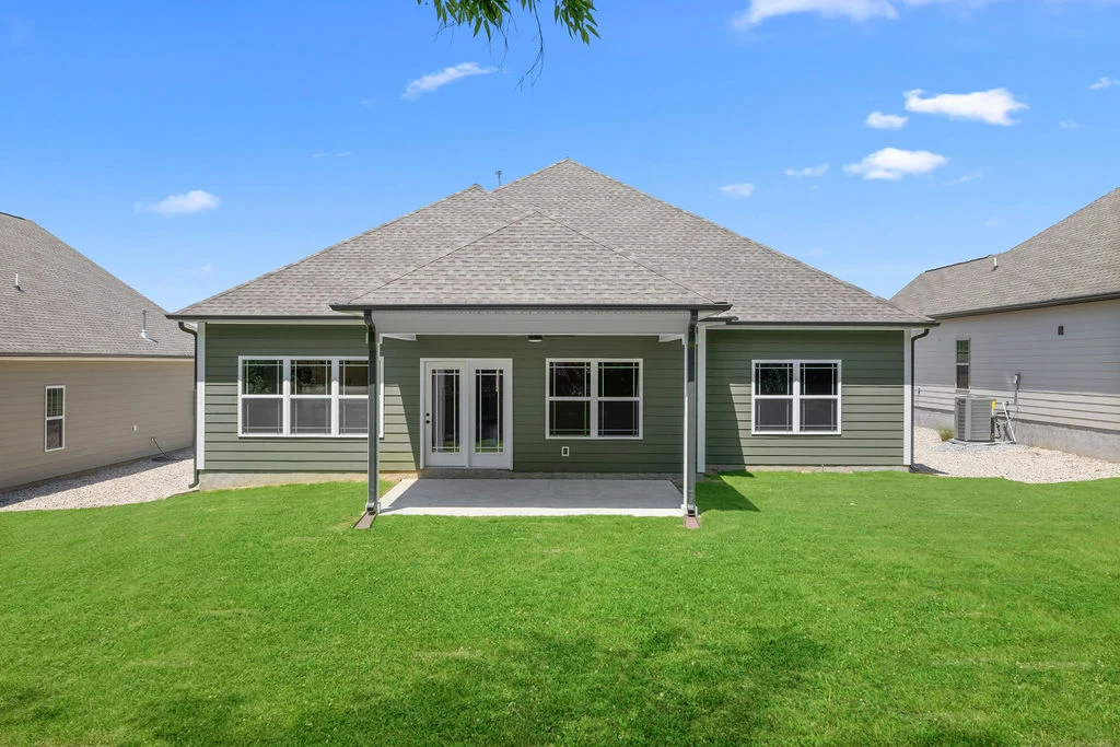 Modern green house with covered patio and spacious lawn. Built by Pratt Home Builders in Chattanooga TN. Bright blue sky above.