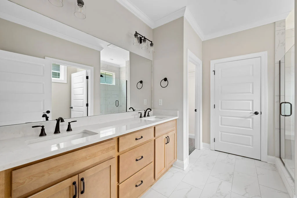 Modern bathroom by Pratt Home Builders in Chattanooga TN, featuring dual sinks, light wood cabinets, marble tiles, and a spacious glass shower.