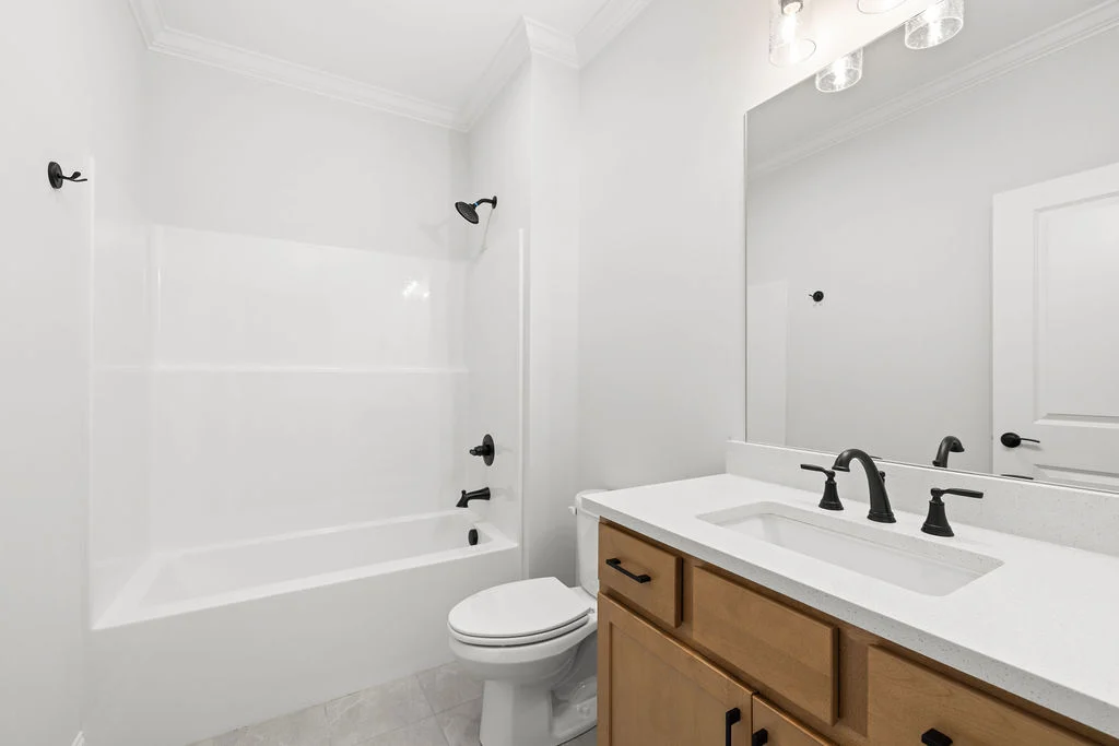 Modern bathroom with white tub, toilet, wooden vanity, and black fixtures, designed by Pratt Home Builders in Chattanooga TN.
