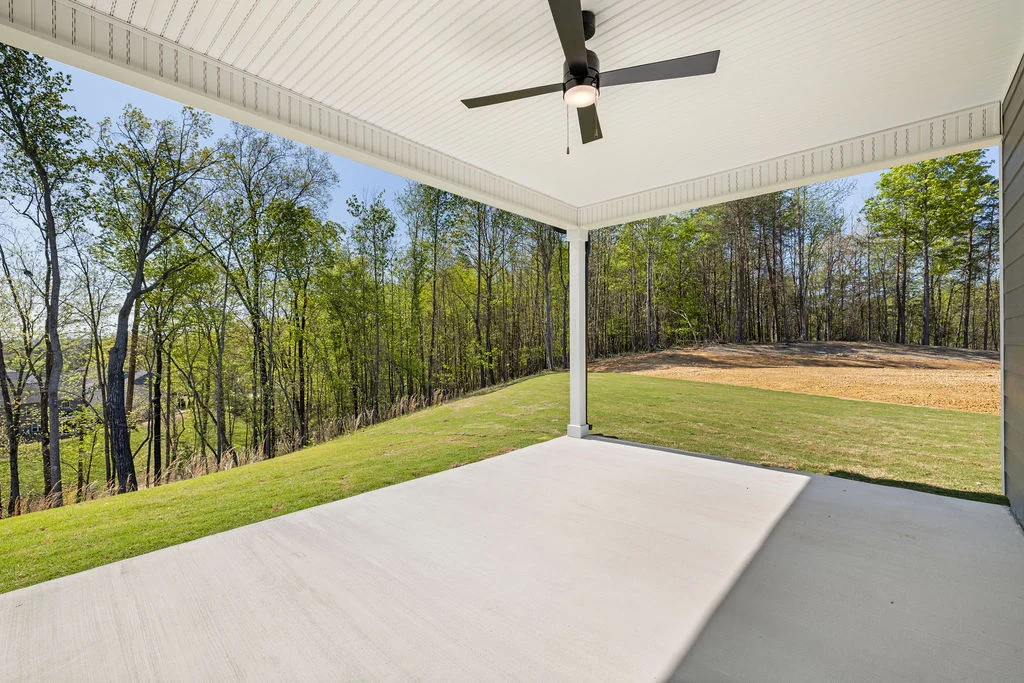 Covered patio with ceiling fan overlooking a grassy yard and wooded area, built by Pratt Home Builders in Chattanooga, TN.