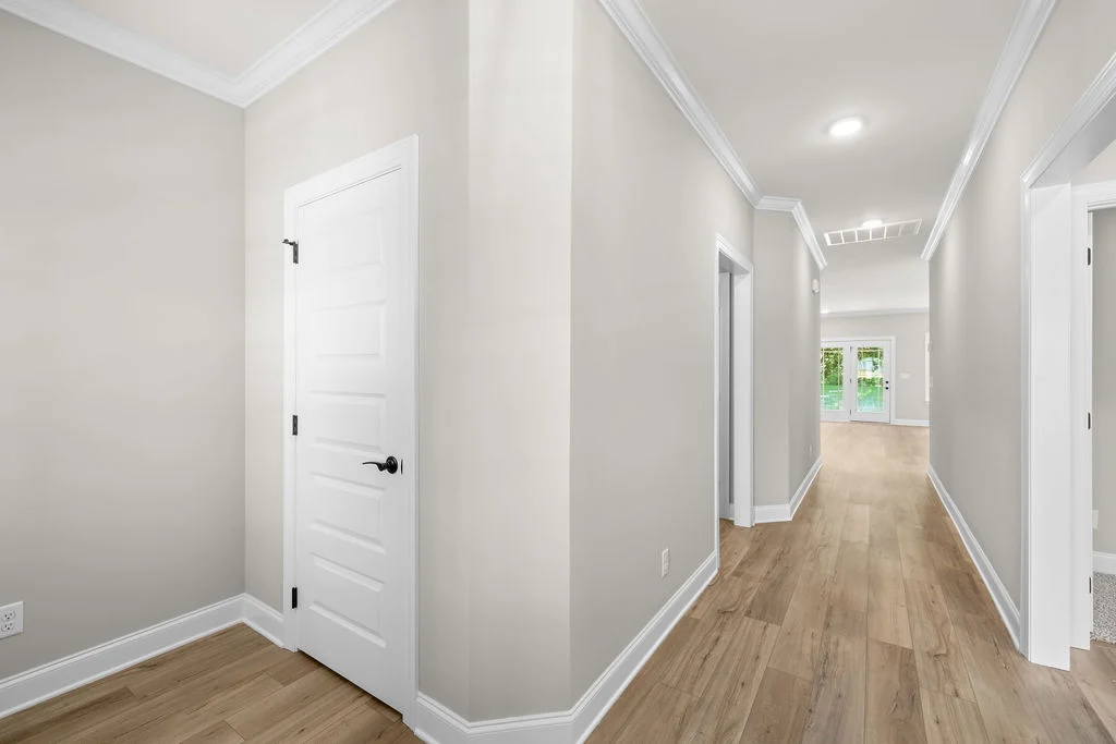 A bright hallway with light wood flooring and white trim leading to a glass door, designed by Pratt Home Builders in Chattanooga TN.